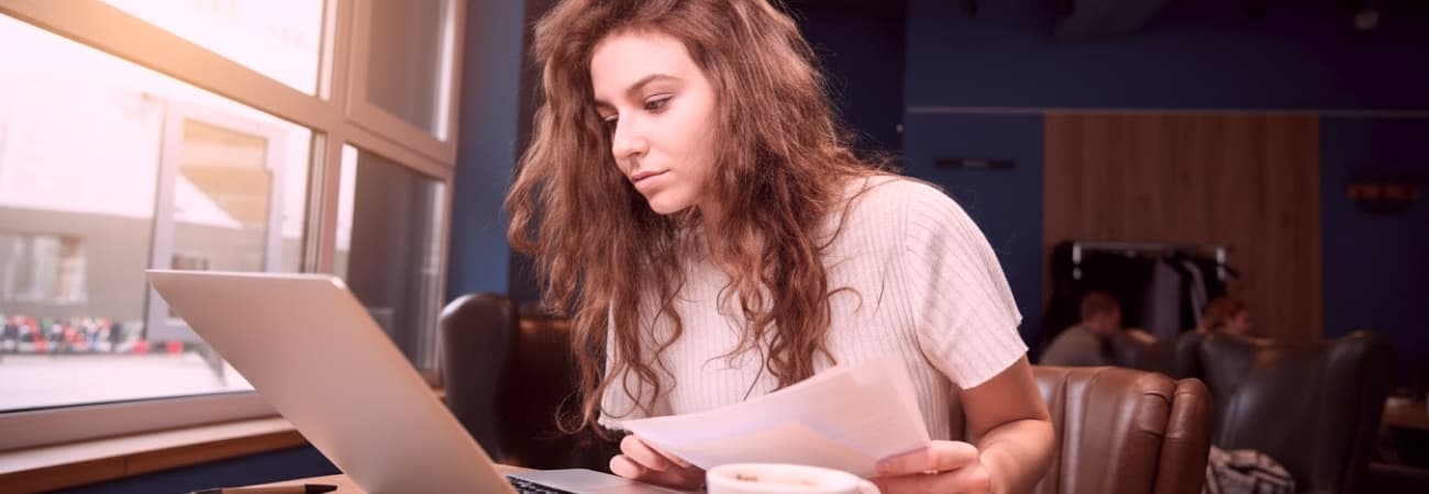 Frau arbeitet am Laptop mit Papieren in einem Café.