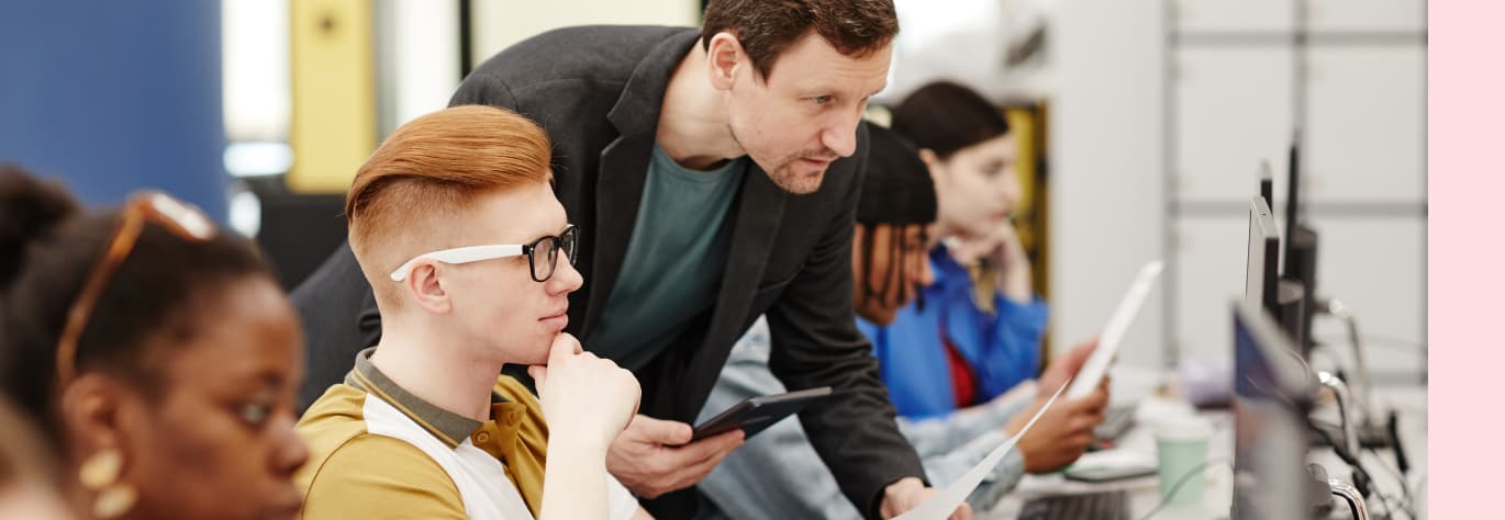 Lehrer unterstützt Schüler bei Computerarbeit im Klassenzimmer.