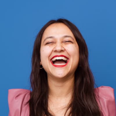 Woman with long dark hair laughing against blue background