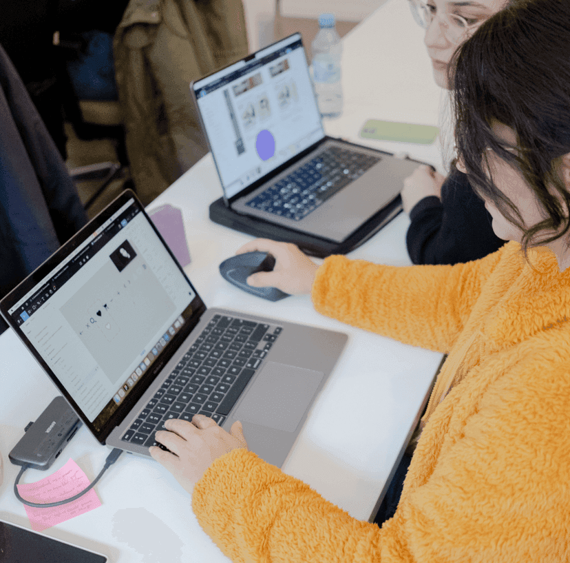 Person working on laptop with another person and laptop in the background.