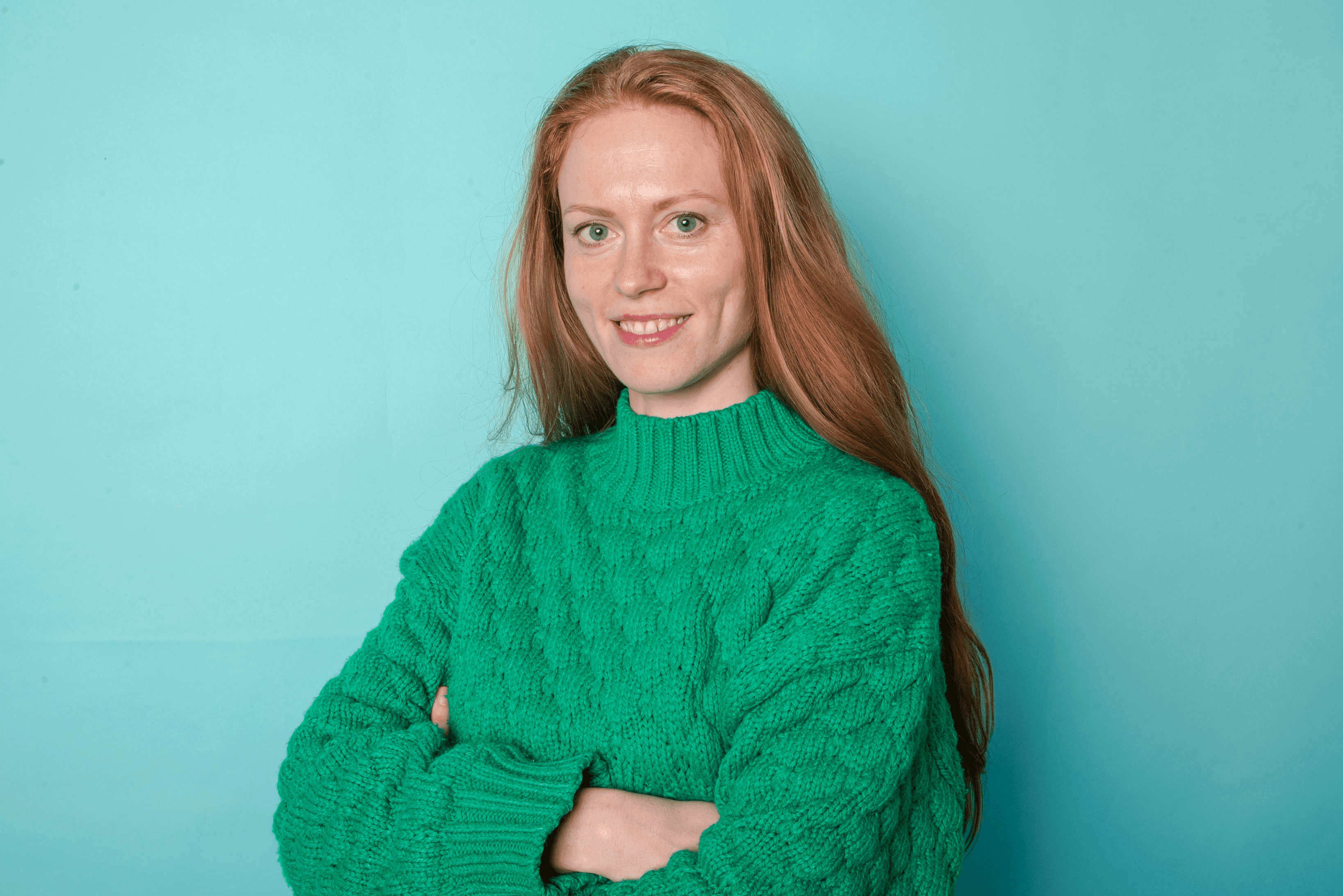 Woman with long red hair in green sweater against turquoise background